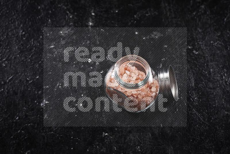 A glass jar full of coarse himalayan salt crystals on black background