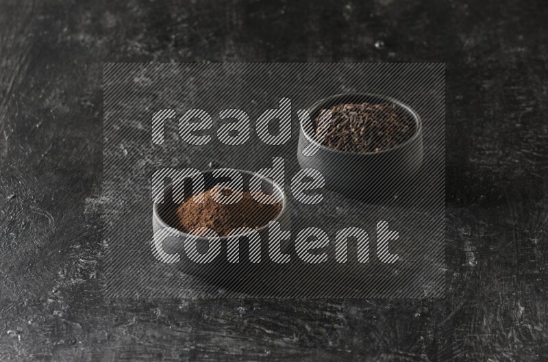 وعاءين من الفخار الأسود أحدهما ممتلئي بحبوب القرنفل والآخر ممتلئ ببودرة القرنفل على خلفية سوداء