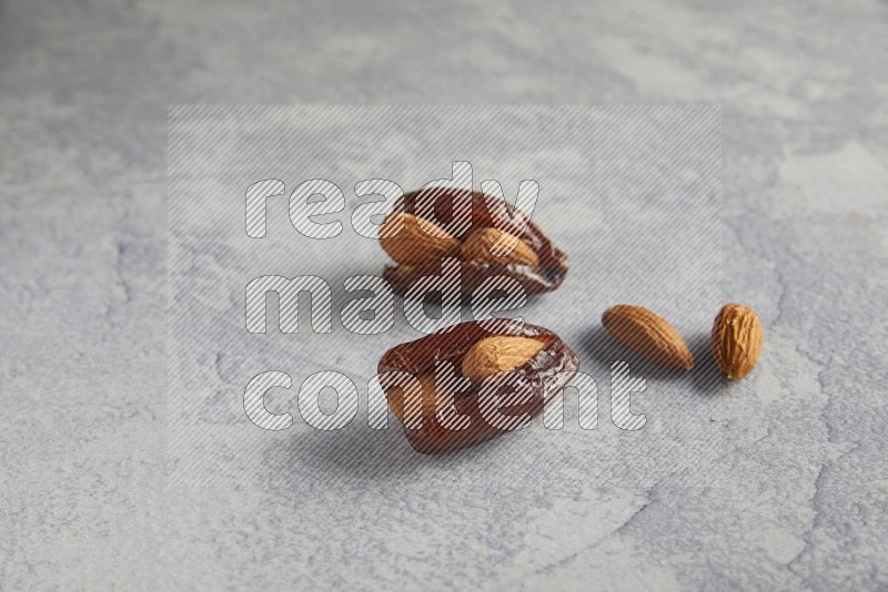 two Almond stuffed date with unroasted  almonds on a light grey background