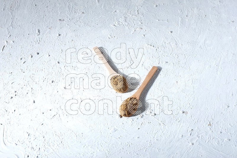 ملاعق خشبية ممتلئة ببودرة بهار الفلفل الحلو مع الحبوب متناثرة على خلفية بيضاء