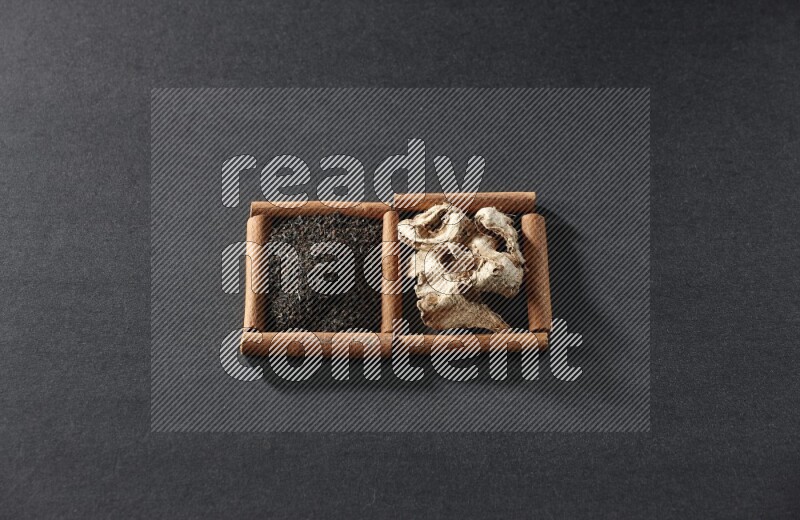 مربعان من أعواد القرفة ممتلئان بالزنجبيل المجفف والشاي الأسود علي خلفية سوداء