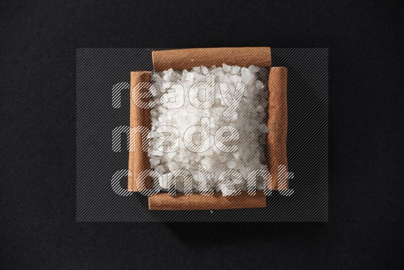 أربعة من أعواد القرفة مكونة شكل مربع بداخلها ملح أبيض علي خلفية سوداء