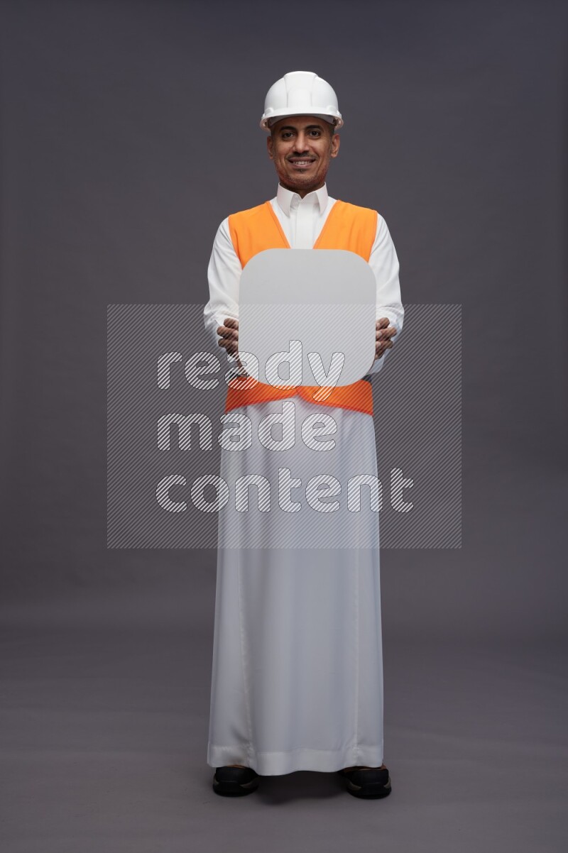 Saudi man wearing thob with engineer vest standing holding social media sign on gray background