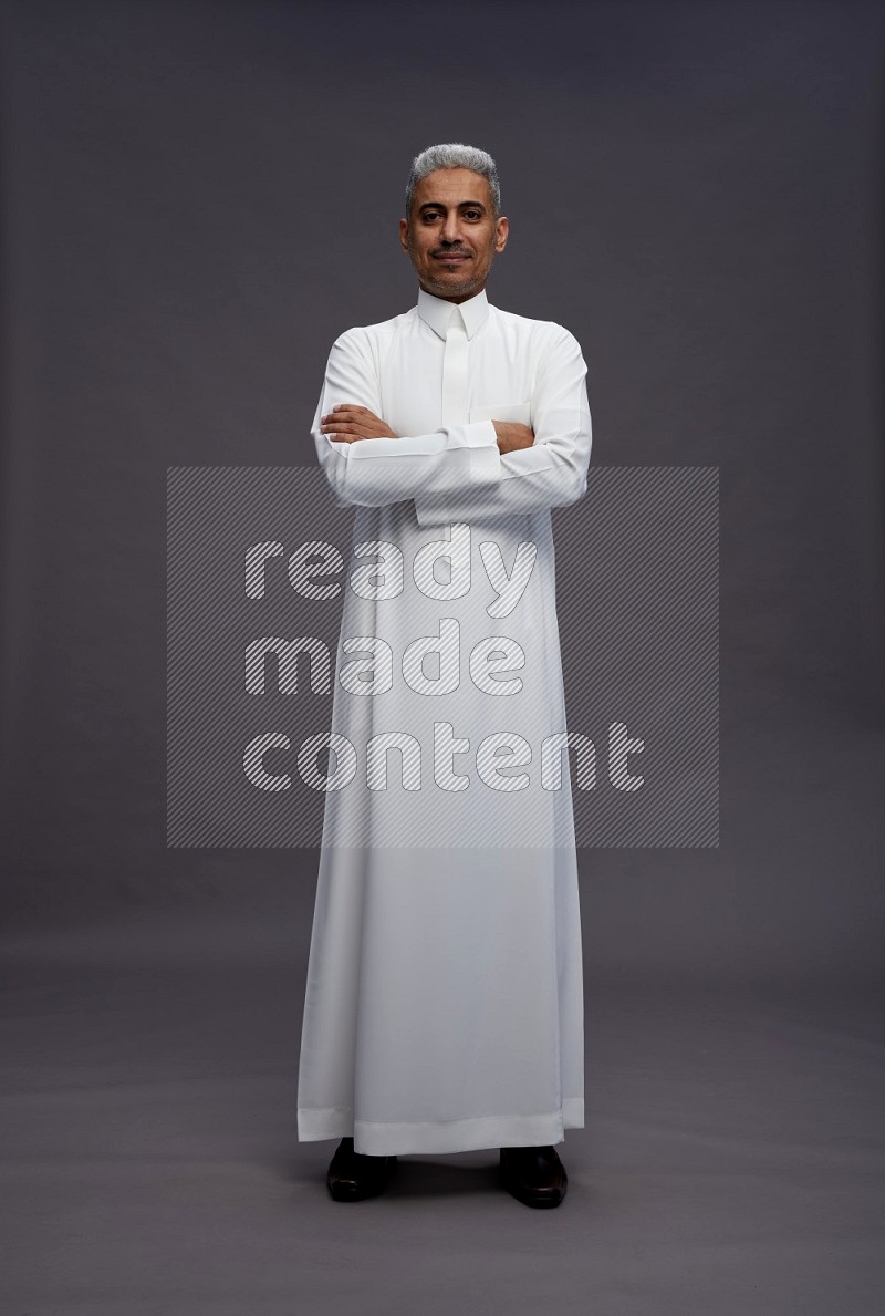 Saudi man wearing thob standing with crossed arms on gray background