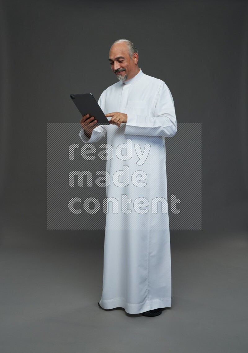 Saudi man without shomag Standing working on tablet on gray background
