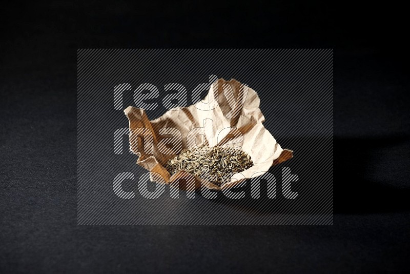 Cumin seeds in a crumpled piece of paper on black flooring