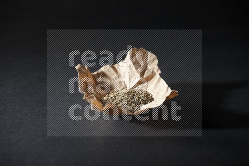 Cumin seeds in a crumpled piece of paper on black flooring