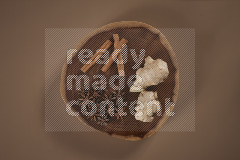 بهارات كاملة متنوعة على صينية خشبية تتضمن زنجبيل طازج ومجفف، أعواد قرفة، هيل، أصابع كركم، قرنفل، يانسون نجمي على خلفية بيج