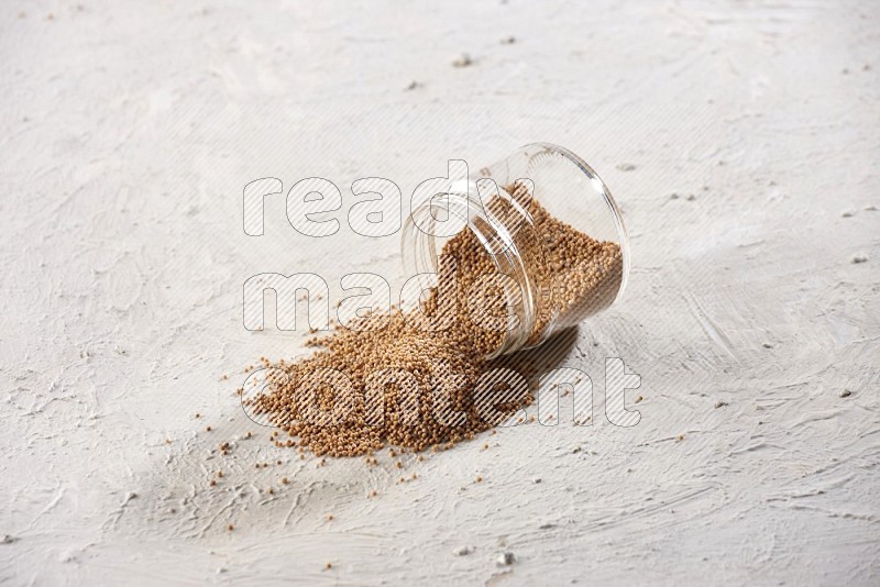A glass jar full of mustard seeds and jar is flipped and seeds spread out on a textured white flooring in different angles