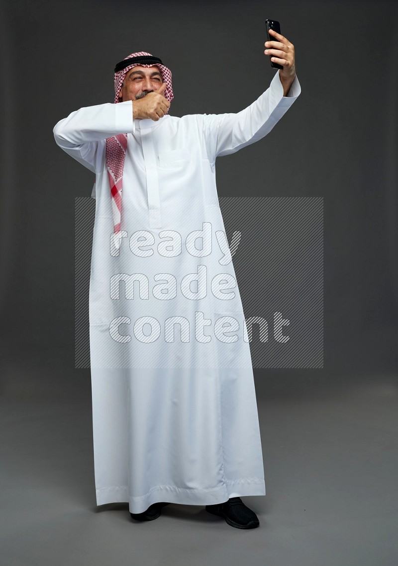 Saudi man with shomag Standing taking selfie on gray background