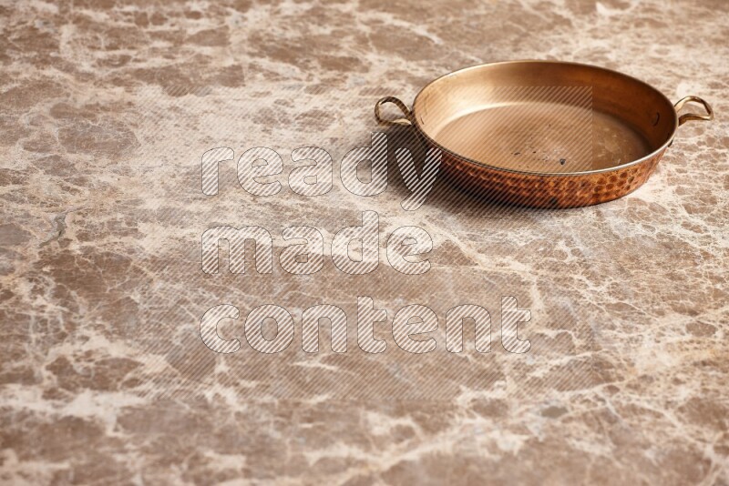 A small copper pan on beige marble background