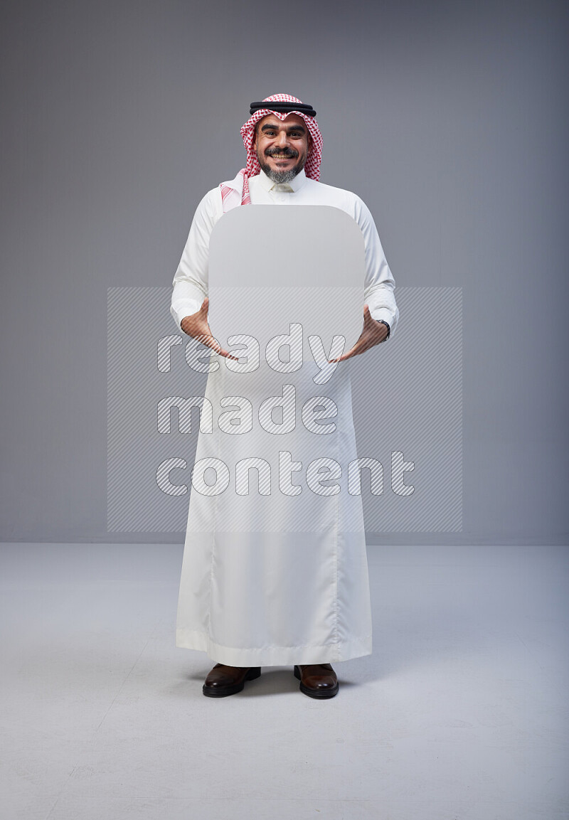 Saudi man Wearing Thob and red Shomag standing holding social media sign on Gray background