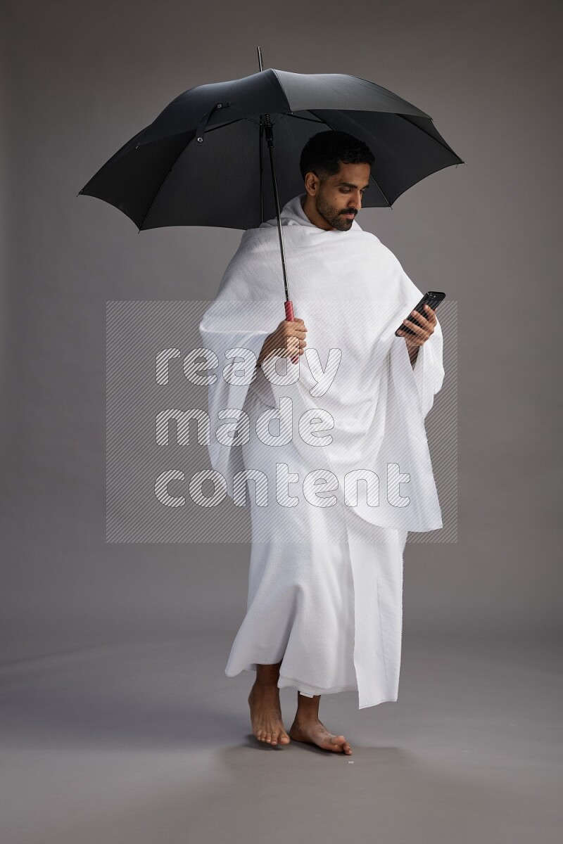 A man wearing Ehram Standing holding umbrella on gray background
