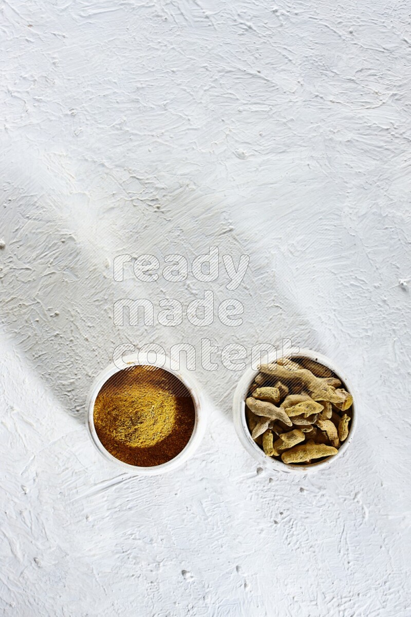 2 beige pottery bowl full of turmeric powder and dried turmeric whole fingers on textured white flooring