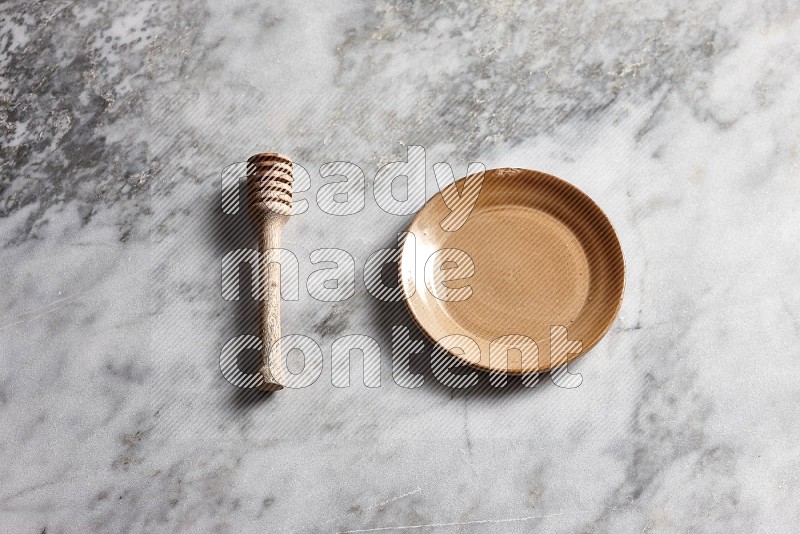 Beige Pottery Plate with wooden honey handle on the side with grey marble flooring, 65 degree angle