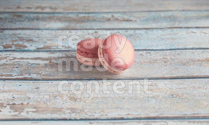 45º Shot of two Pink Litchi Raspberry macarons on light blue wooden background