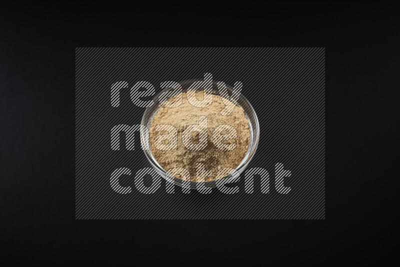 A glass bowl full of ground ginger powder on black background