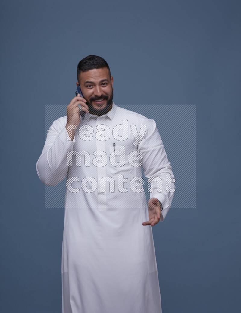 A Saudi man calling on blue background wearing Saudi Thob