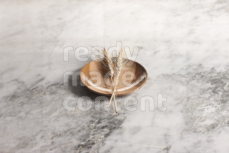 Wheat stalks on multicolored pottery plate on grey marble background