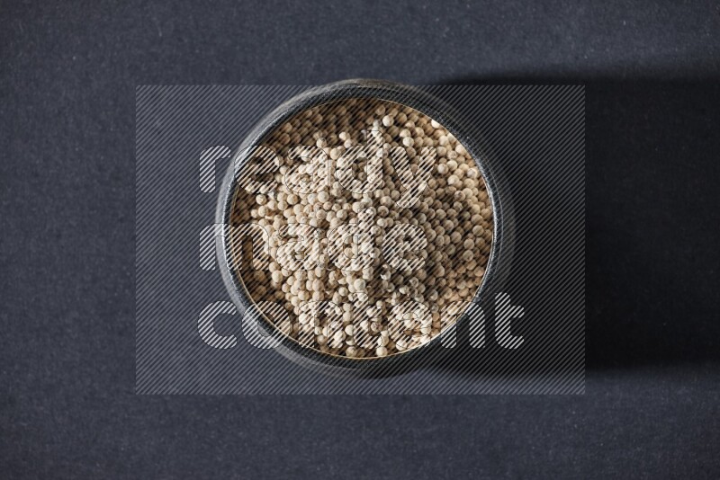 Black pottery bowl full of white pepper on black flooring