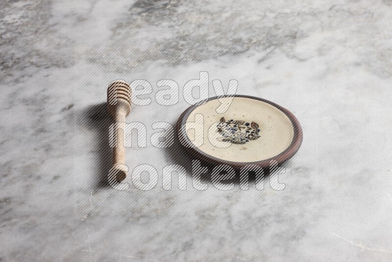 Decorative pottery plate with wooden honey dipper on the side on grey marble background