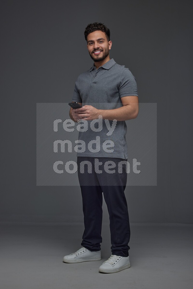 A man wearing casual standing and using his phone eye level on a gray background