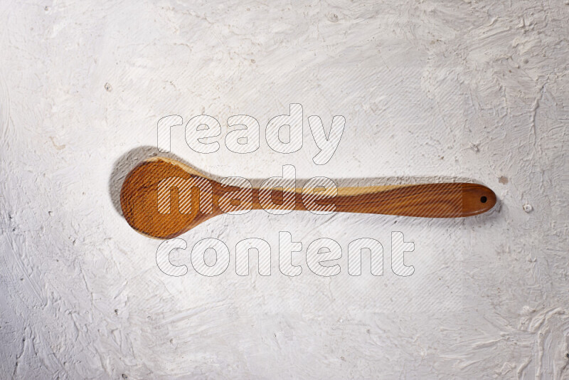 A wooden ladle full of ground paprika powder on white background