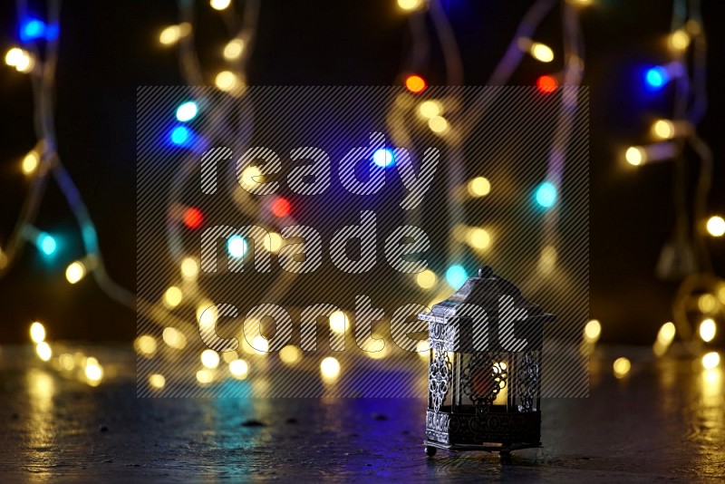 A silver lantern with fairy light in a dark setup