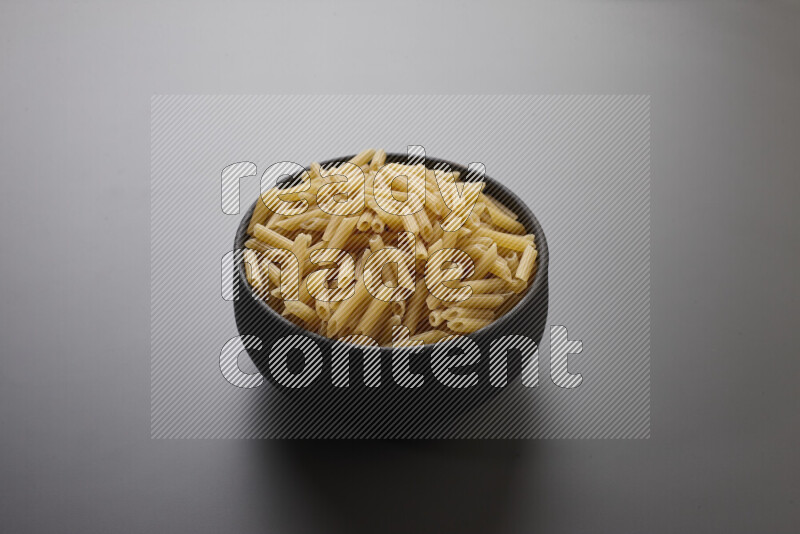 Mini penne pasta in a pottery bowl on grey background
