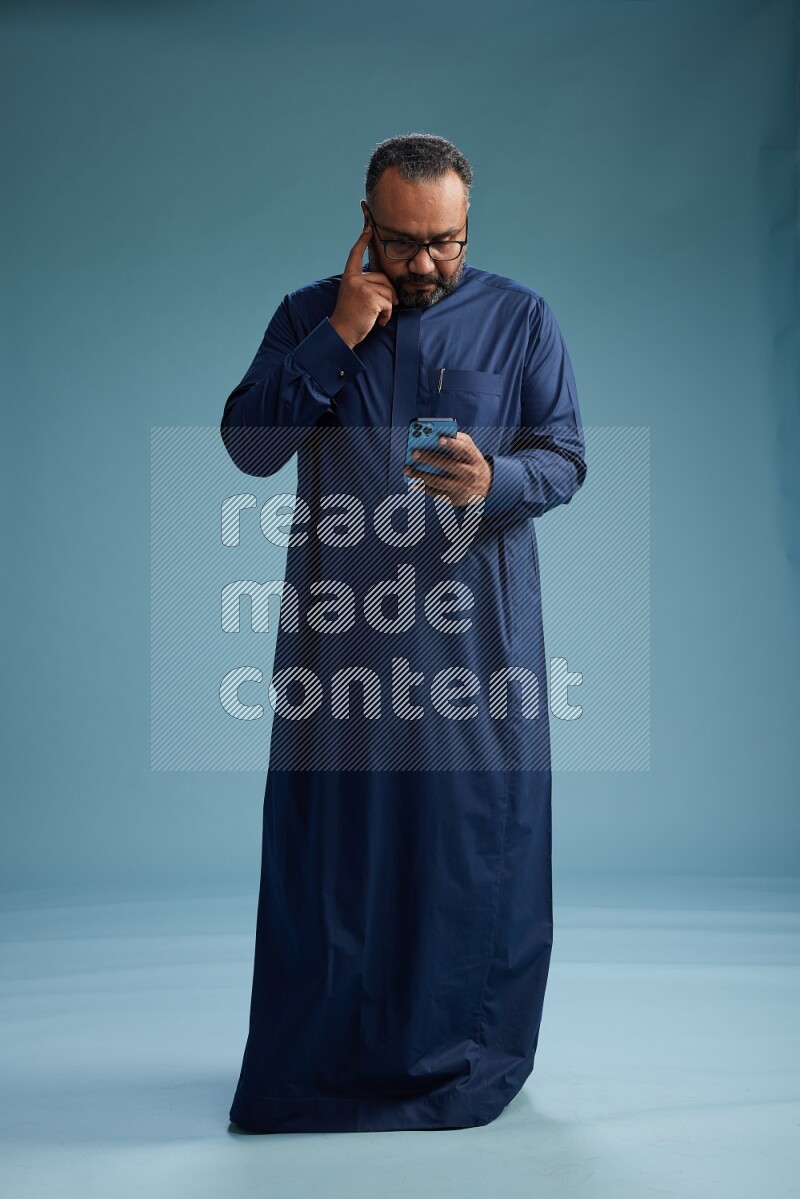 Saudi Man without shimag Standing texting on phone on blue background
