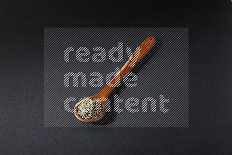 A wooden ladle full of cumin seeds on black flooring
