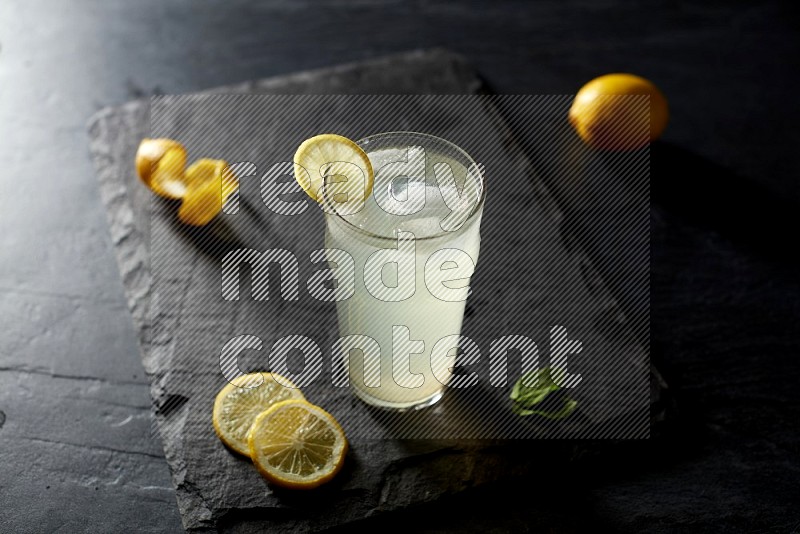 A glass of lemon juice with a lemon slice on black background