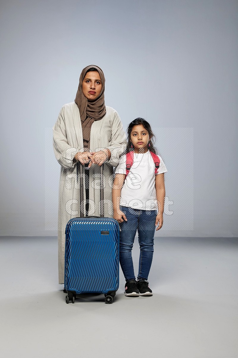 Mom and daughter standing pulling a carry-on bag on gray background