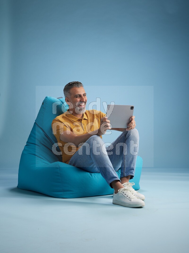 A man sitting on a blue beanbag and working on tablet