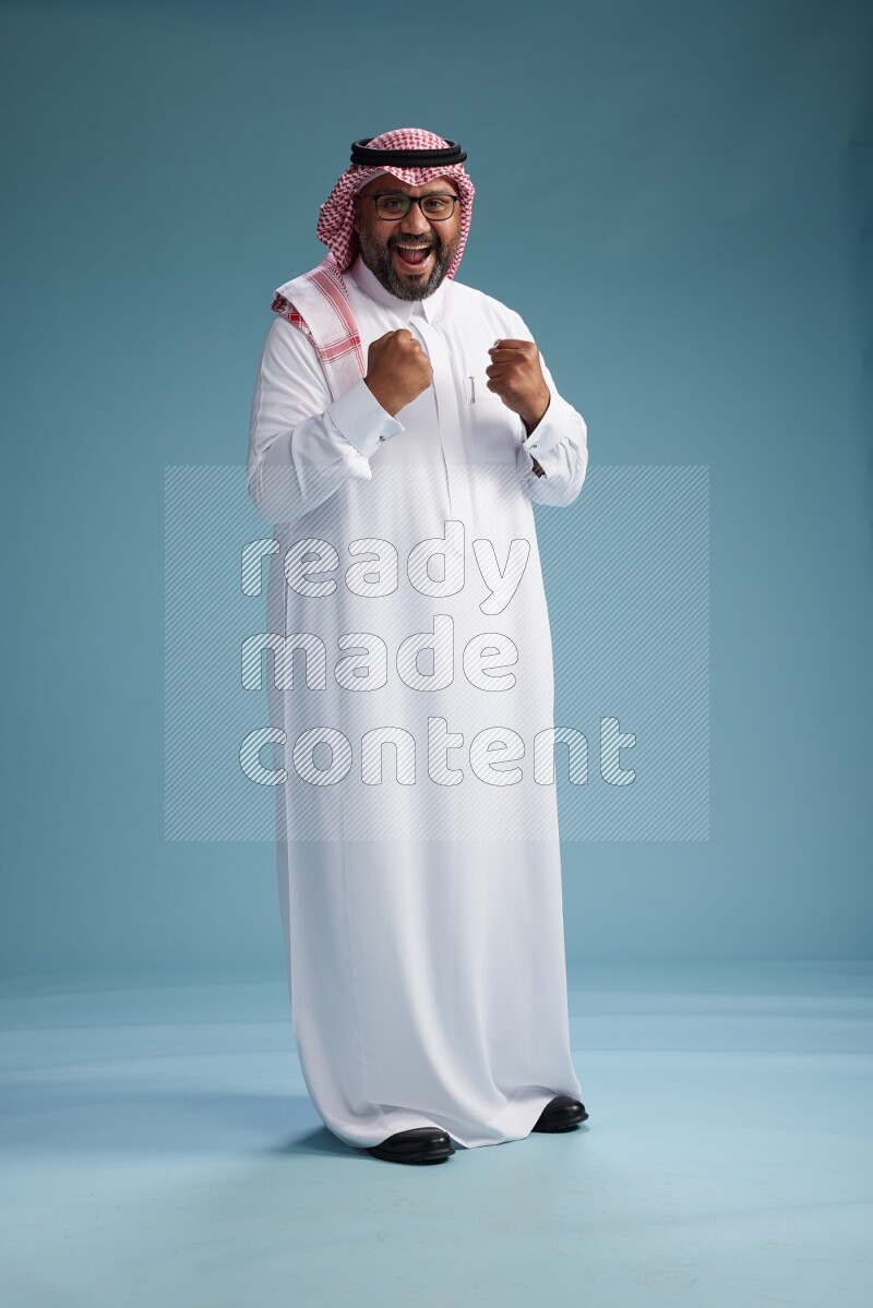 Saudi Man with shimag Standing Interacting with the camera on blue background