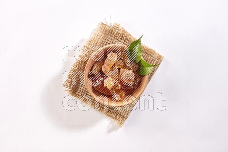 A wooden bowl full of gum arabic on a piece of burlap on white flooring