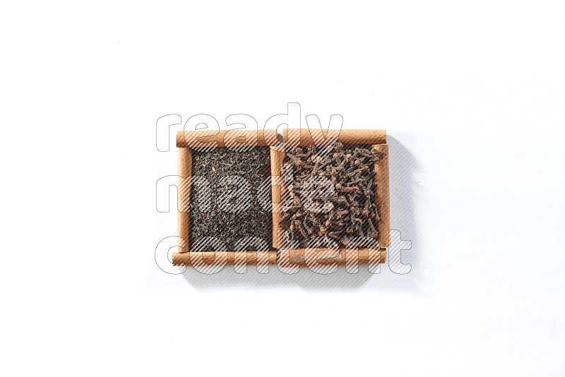 مربعان من أعواد القرفة ممتلئان بالشاي الأسود وحبوب القرنفل علي خلفية بيضاء