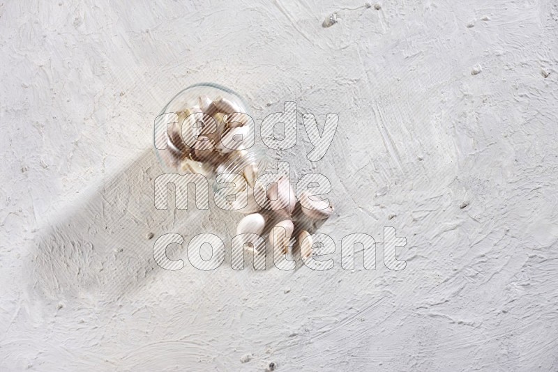 A glass spice jar full of garlic cloves flipped and the cloves came out on a textured white flooring in different angles