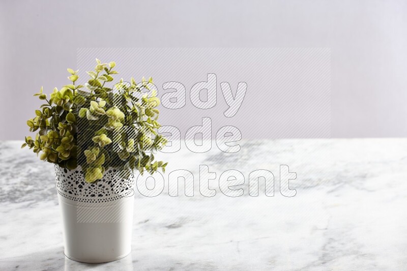 Green artificial plant in white decorative pot on grey marble background