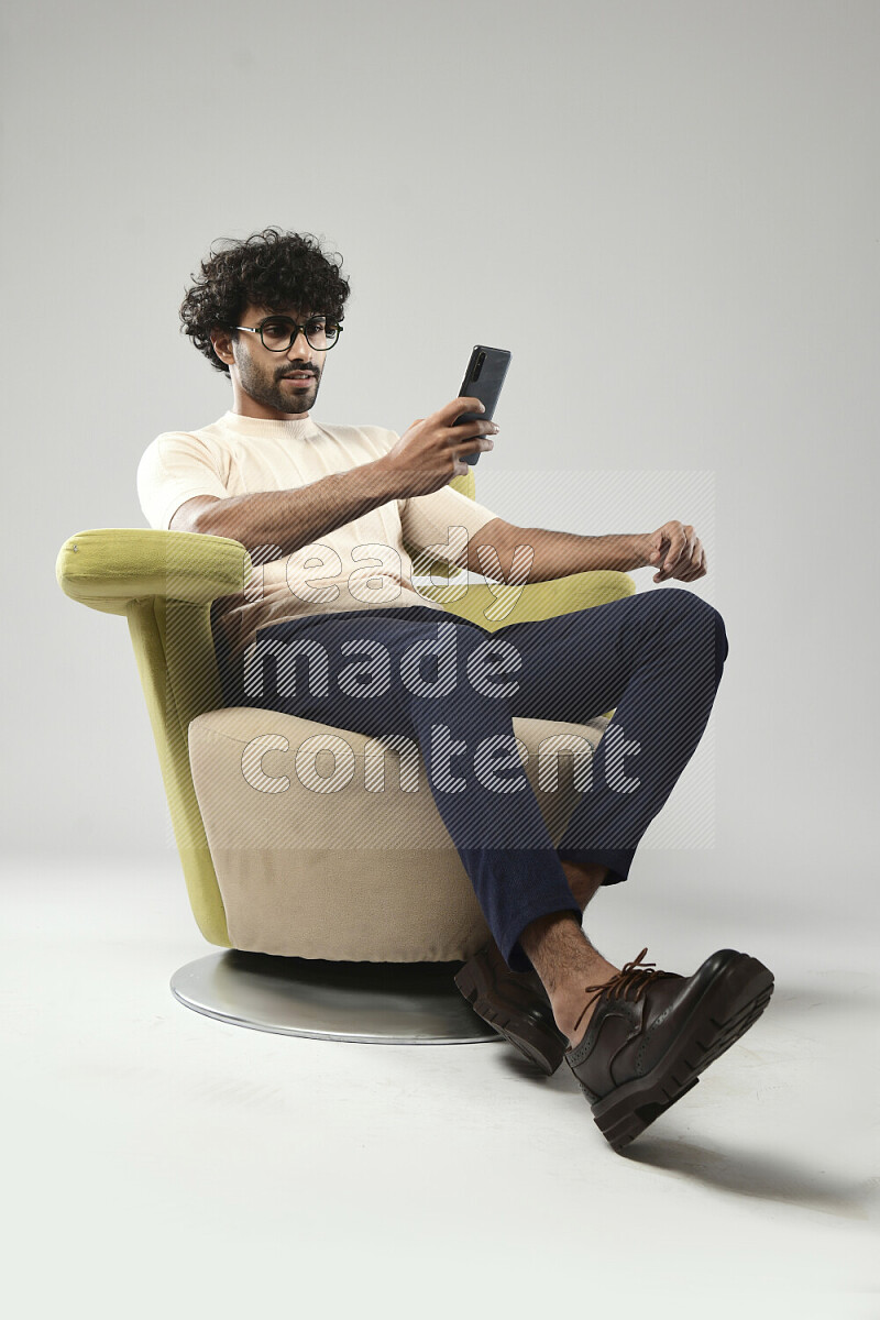 A man wearing casual sitting on a chair browsing on the phone on white background