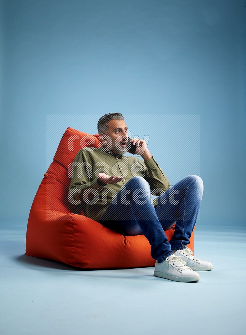 A man sitting on an orange beanbag and talking on the phone