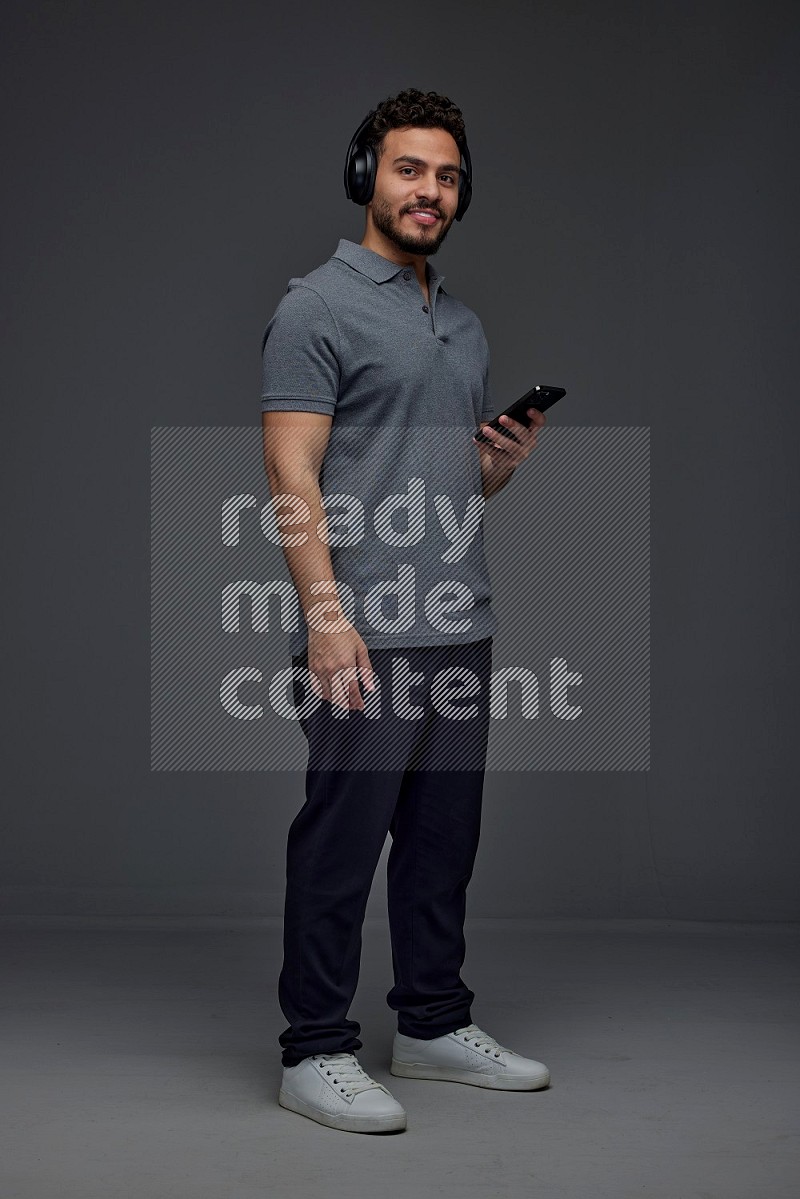 A man wearing casual and using his phone and headphone eye level on a gray background