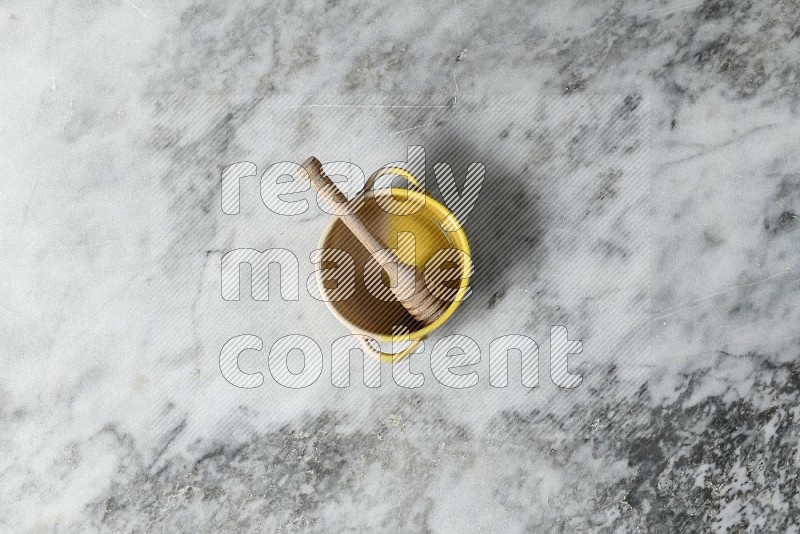 Multicolored Pottery Bowl with wooden honey handle in it, on grey marble flooring, Top View