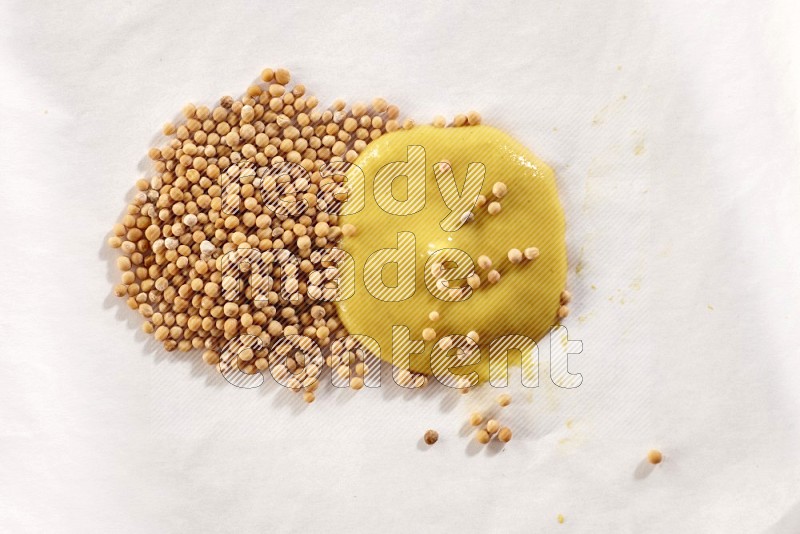 Mustard seeds and mustard paste on a piece of white paper on white flooring