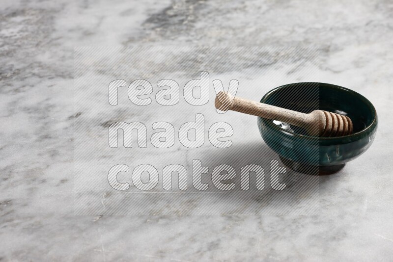 Dark green pottery plate with wooden honey dipper in it on grey marble background