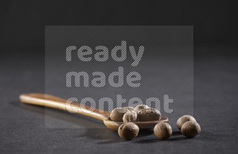 A wooden ladle full of whole nutmeg seeds on a black flooring