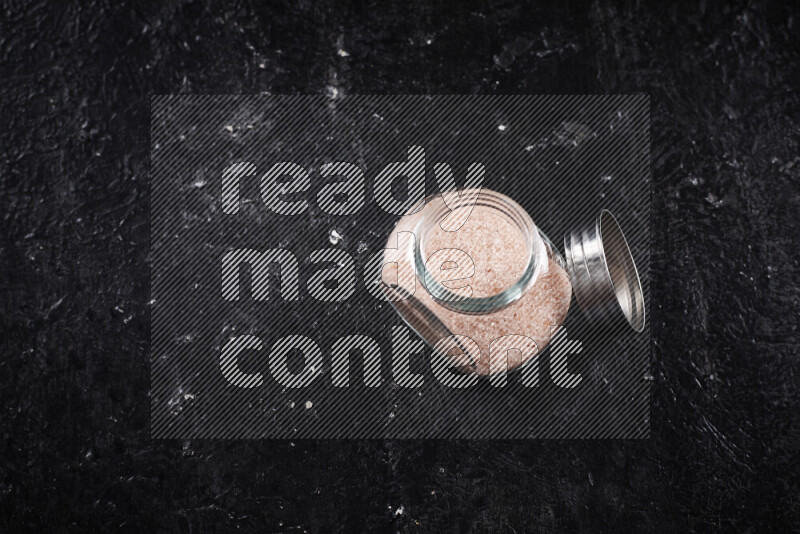 A glass jar full of fine himalayan salt on black background