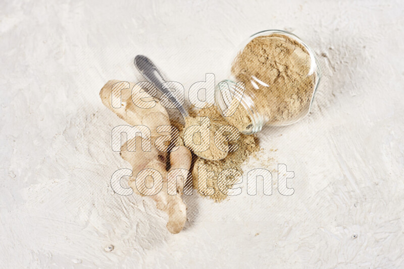 A glass jar full of ground ginger powder flipped with some spilling powder on white background