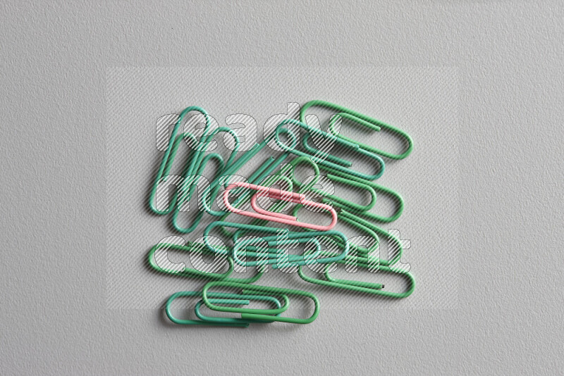 A pink paperclip surrounded by bunch of green paperclips on grey background