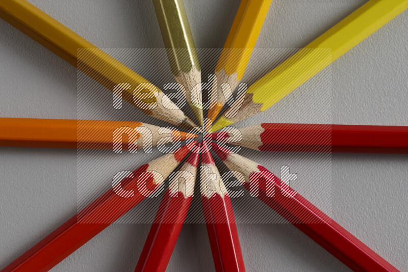 An arrangement of colored pencils in shades of yellow, orange and red on grey background